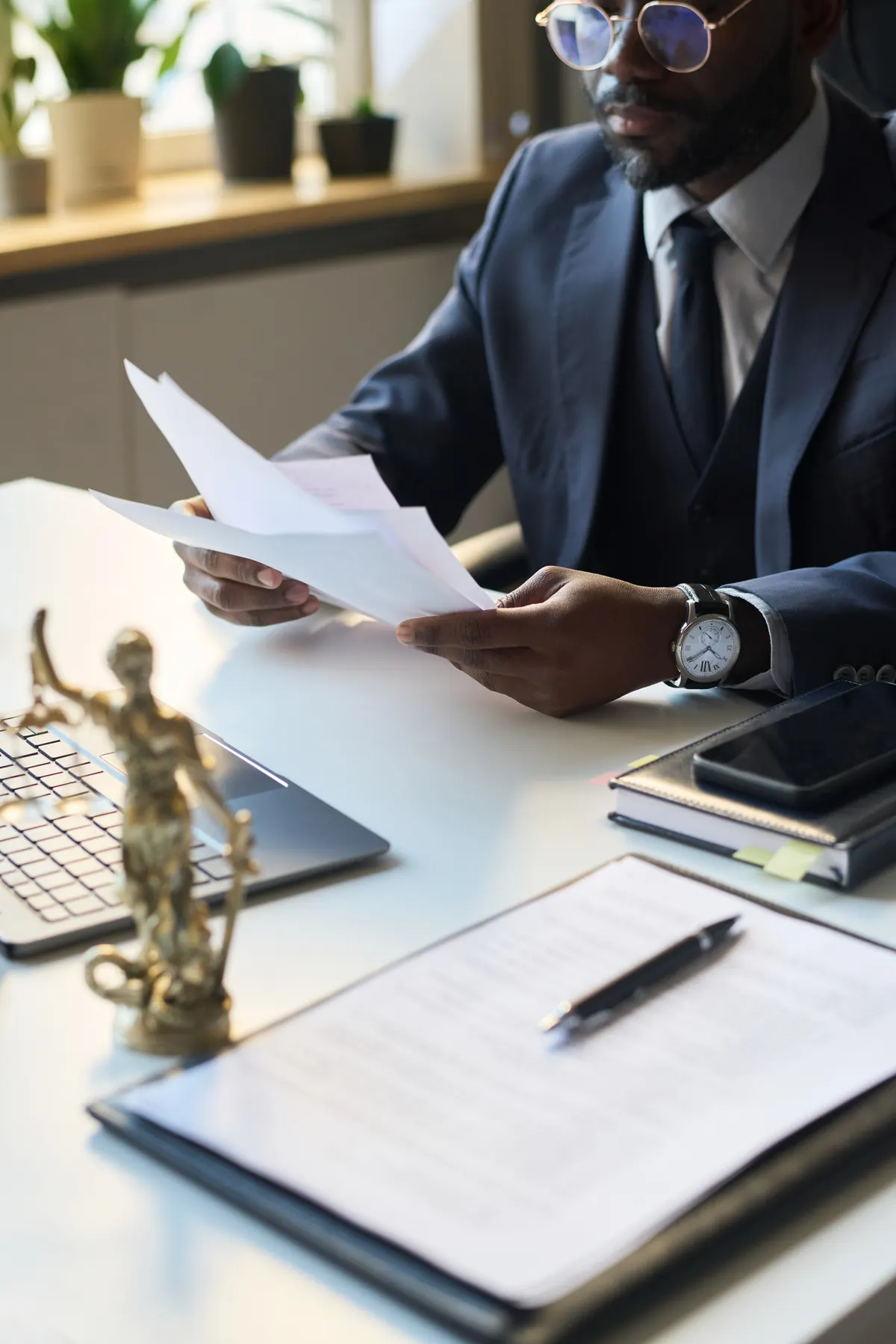 Lawyer reviewing documents at a desk beside a scales of justice statue