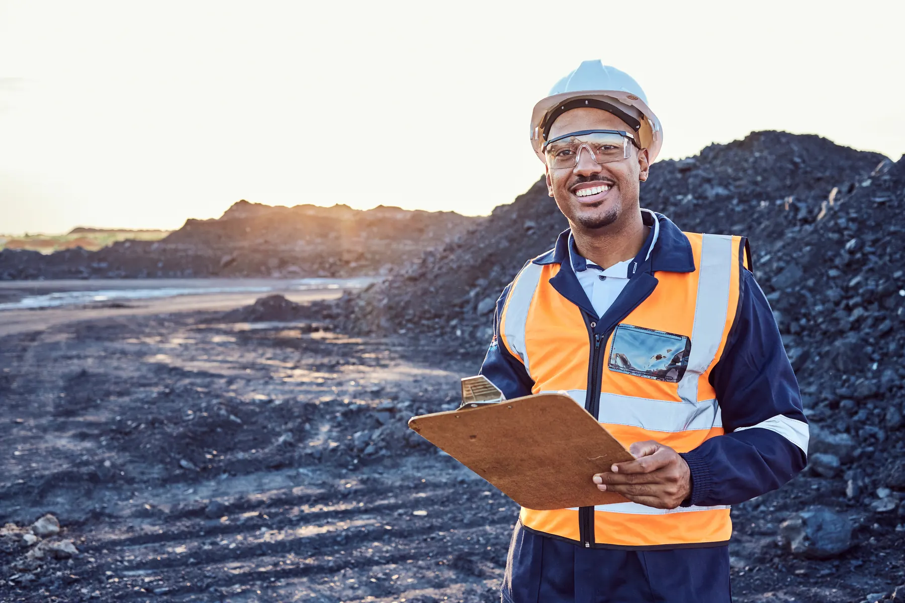 Mine worker in a hard hat holding a clipboard at a mining site